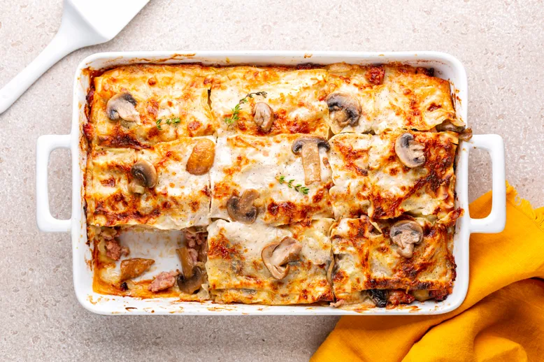 Plat à gratin de lasagnes aux champignons et sauce crémeuse, coupées en portions.